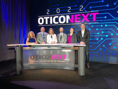 Six smiling people in business clothing standing behind podium at 2022 OticoNext event