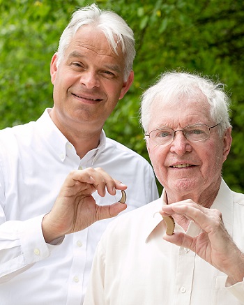 Unitron President Jan Metzdorff holding Moxi Kiss RIC with Unitron founding partner Rolf Dohmer holding a 205A BTE from 1966