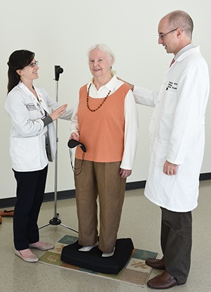 Timothy Hullar MD and medical student Miranda Colletta help patient Audrey Miller prepare for a balance test
