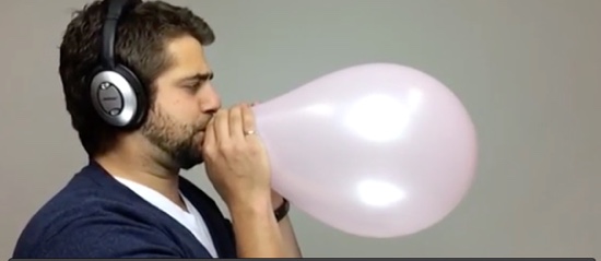 man blowing up balloon with headphones on