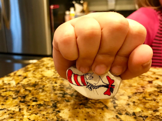 Infant Palmar grasp demonstrated with a child hand holding a cat in the hat eraser