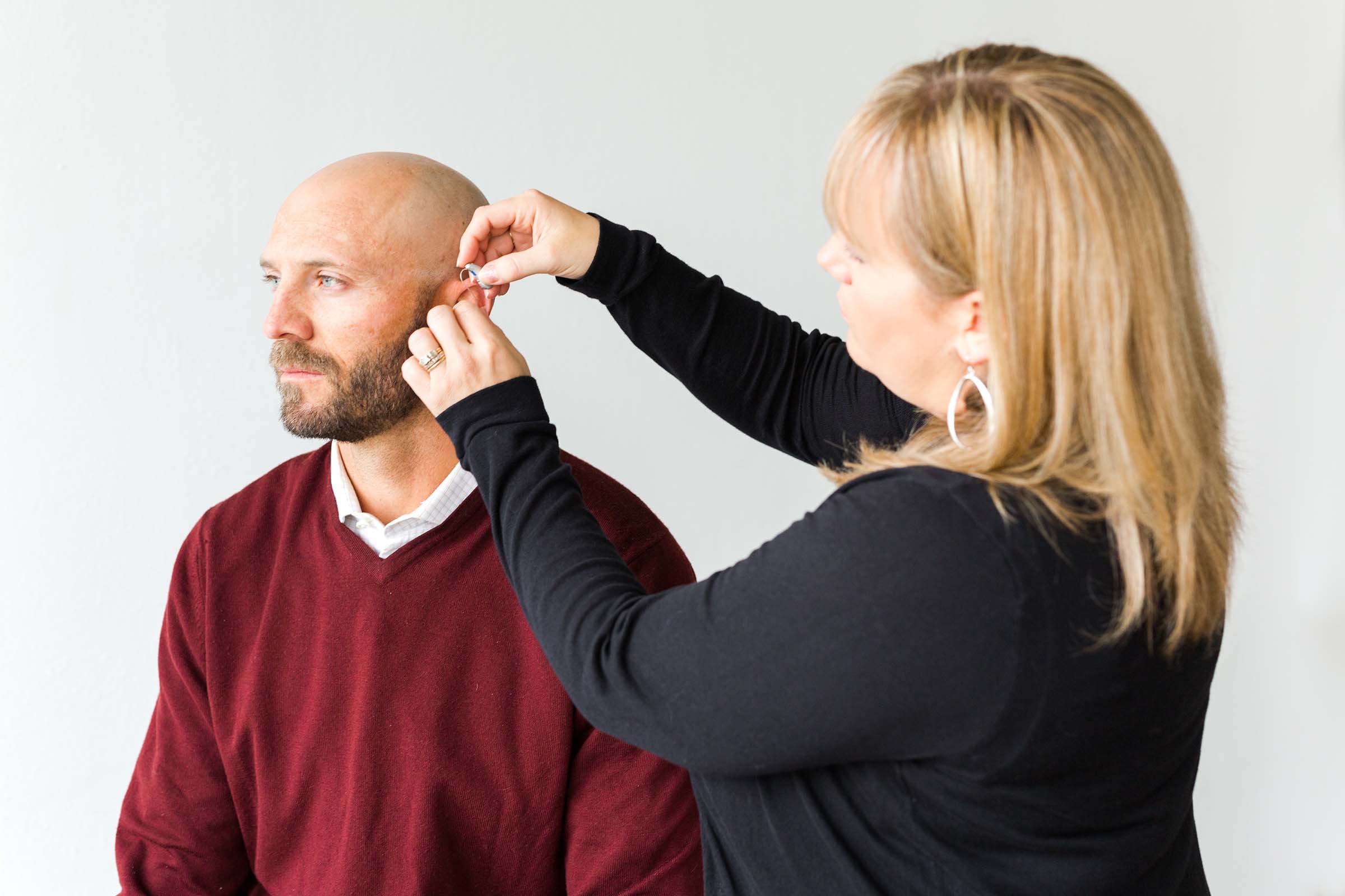 Woman fitting man with hearing aid