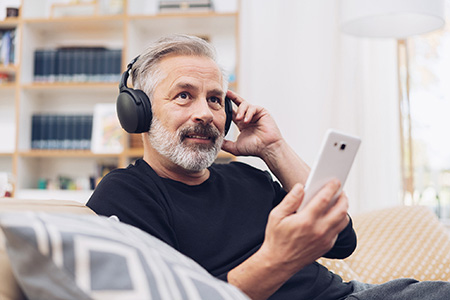 Man sitting on a couch with headphones on and a cellphone in hand