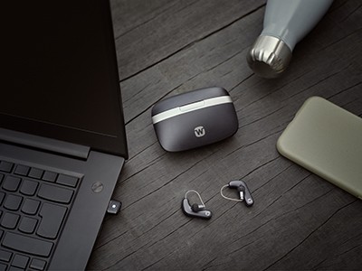 RIC hearing aids, case and laptop on a table