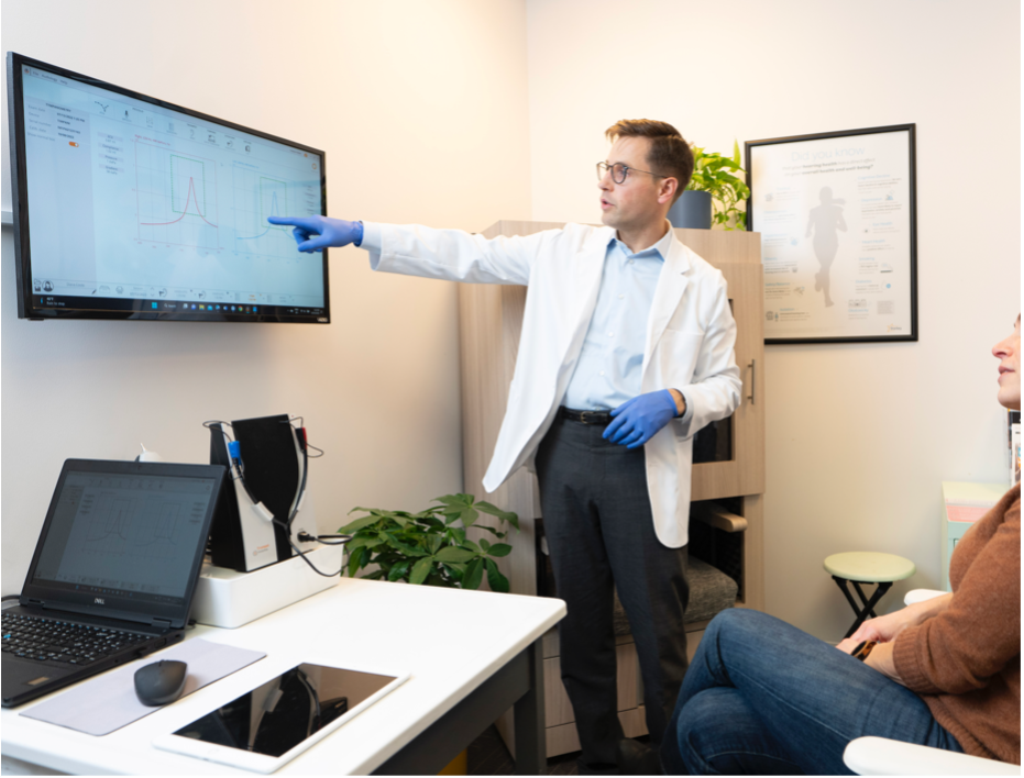 man in white coat pointing at large wall mounted computer screen 